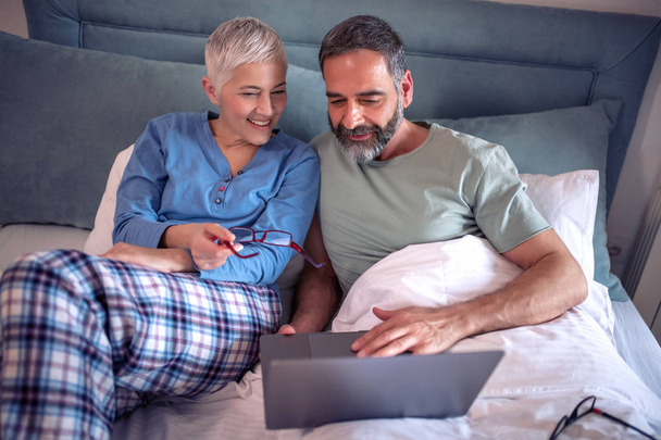 Senior couple using laptop in bedroom. - Foto, Imagem