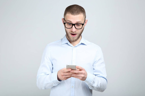 Young man in glasses with smartphone on grey background - Фото, изображение