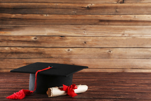 Graduation cap with diploma on brown wooden table - Valokuva, kuva