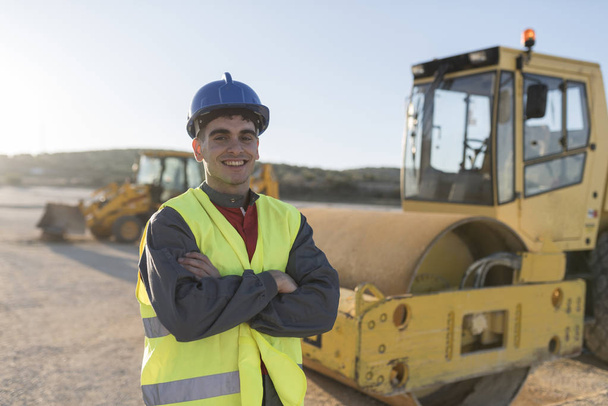 Young man posing in construction outdoors site with vehicle in background - Фото, изображение