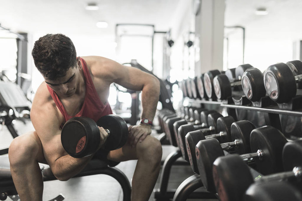 Man training biceps in gym near to dumbbells - Фото, зображення