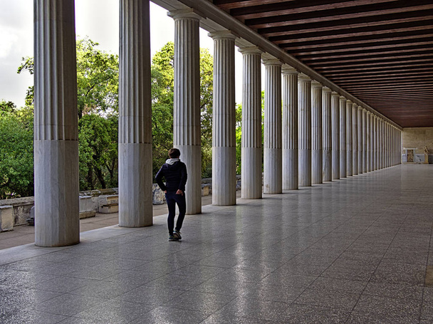 Stoa of Attalos in Athens, Greece. Impressive building in Ancient Agora archeological site. Woman walking away from the camera. Great perspective from columns. - Photo, Image