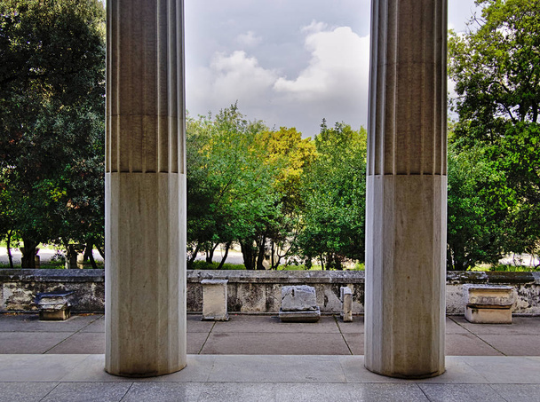 View of trees and cloudy sky behind two columns in Stoa of Attalos in Athens, Greece. Impressive building detail in Ancient Agora archeological site. - Photo, Image