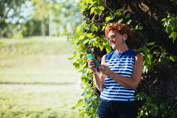 Dospělá žena naslouchající hudbě na sluchátkách v parku - Fotografie, Obrázek