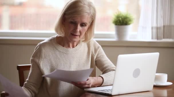 Smiling old mature lady paying bills online on laptop - Filmati, video