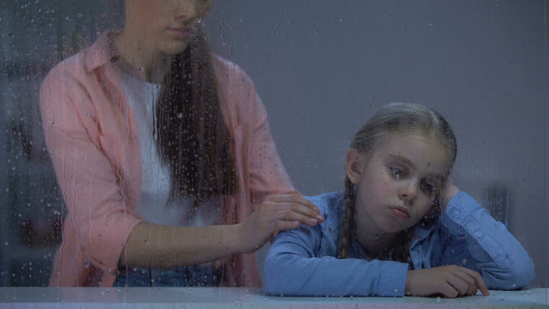 Moeder steunt klein meisje achter regenachtig venster, Kid lijdt aan pesten - Video