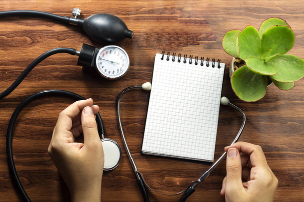 medische concepttekst schrijven op witte notebook en zwarte stethoscoop, sfygmomanometer op houten tafel - Foto, afbeelding