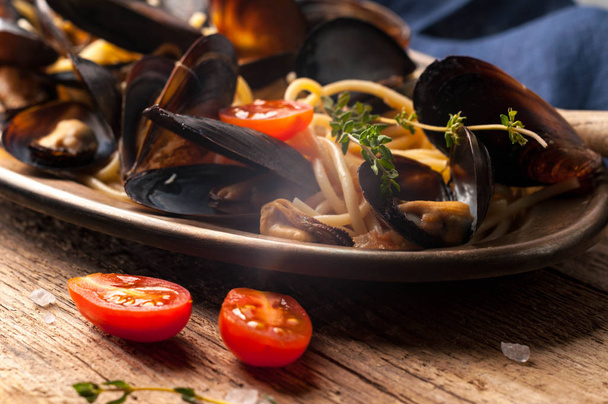 close up of metal golden plate with delicious traditional italian spaghetti and mussels cooked in sauce with tomatoes on wooden background - Foto, Imagem