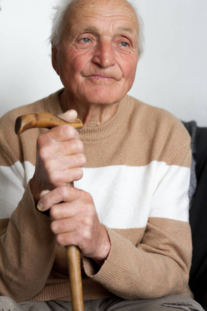 Retrato de um velho sorridente que colocou as mãos no punho de uma bengala de madeira
. - Foto, Imagem