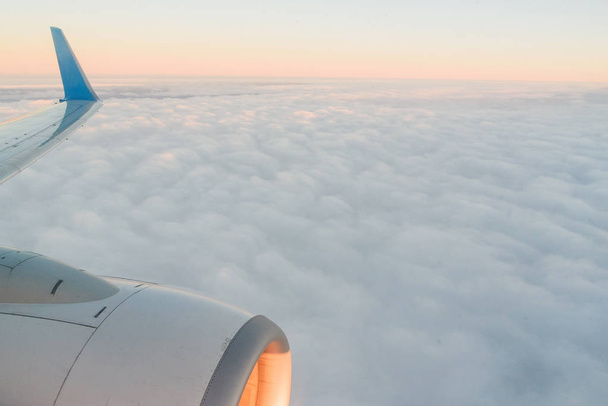 The view from the airplanes illuminator to the wing, airplane turbine and fluffy clouds at sunrise. Flying over the clouds - Foto, Imagen