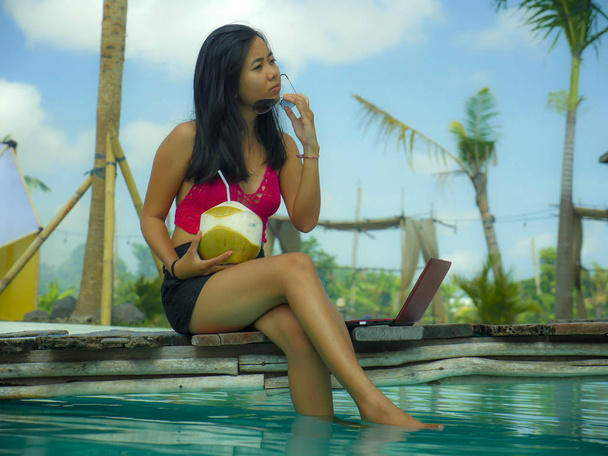 young beautiful and happy Asian Indonesian teenager woman in bikini at tropical resort swimming pool networking relaxed and chilled with laptop computer smiling - Photo, image