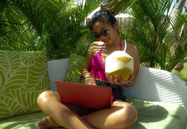 lifestyle outdoors portrait of young happy and attractive Asian Indonesian teenager girl in bikini networking with laptop computer at tropical resort garden bed - Photo, Image