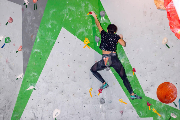 Rock climber woman hanging on a bouldering climbing wall, inside on colored hooks - Photo, Image