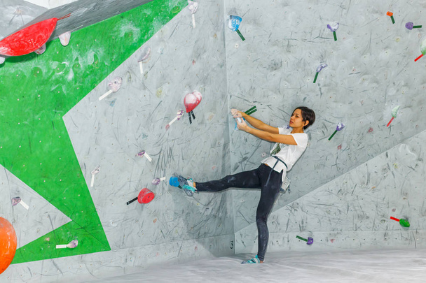 Rock climber woman hanging on a bouldering climbing wall, inside on colored hooks - Fotó, kép