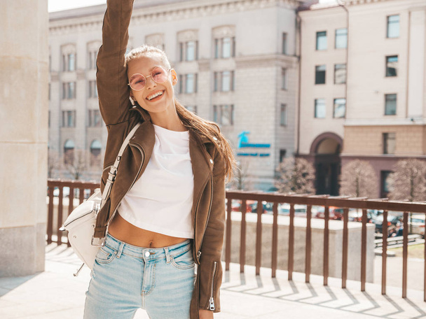 Portrait of beautiful smiling brunette model dressed in summer hipster jacket clothes. Trendy girl posing in the street background. Funny and positive woman in round sunglasses - Fotó, kép