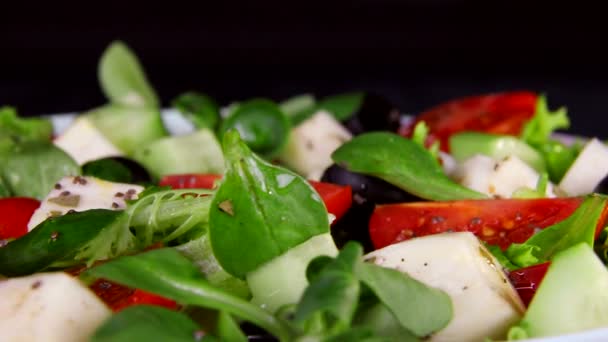 Egészséges táplálkozás. Saláta zöldséggel és szelet sajtparadicsom és uborka. Plate közeli forog a fekete háttér - Felvétel, videó