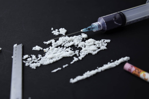Cocaína e Rupia Indonésia pronto para usos em mesa escura. Foco seletivo na seringa
 - Foto, Imagem