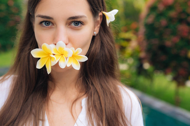 Portret pięknej dziewczyny z naturalnego makijażu i plumeria, kwiatów frangipani w jej ustach. - Zdjęcie, obraz