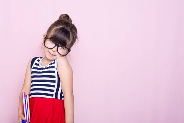 Retrato de una niña sonriente con gafas grandes graciosas. Escuela y preescolar. Moda. Estudio retrato sobre fondo rosa
. - Foto, Imagen