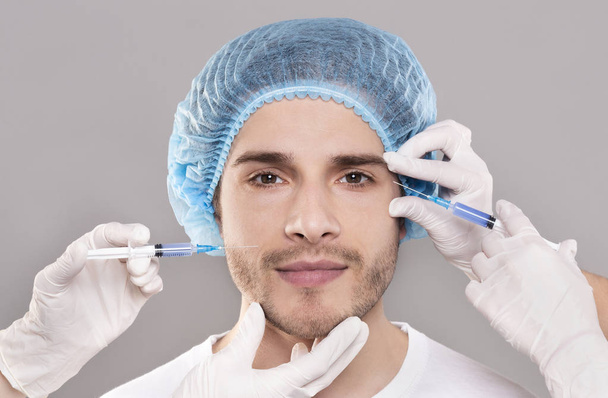 Mans face and beauticians hands with syringes making beauty injections - Valokuva, kuva