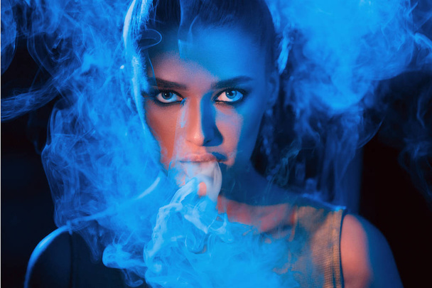 Young woman smoking vape or e-cigarette in neon light - Foto, afbeelding