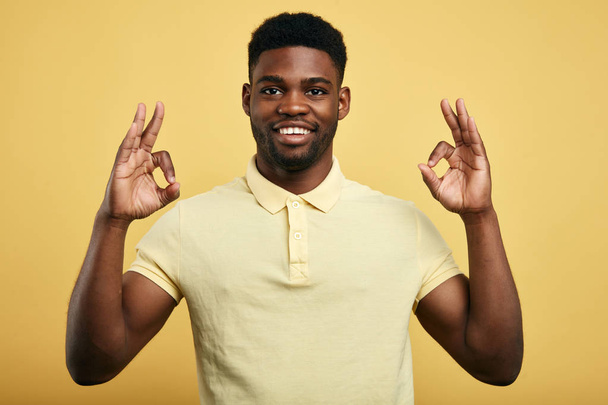 positive guy shows OK gesture on a yellow background. - Φωτογραφία, εικόνα