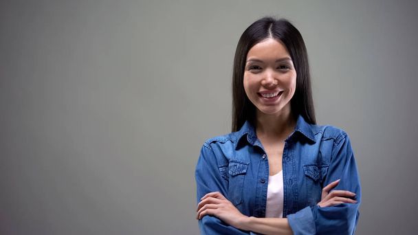Smiling young asian woman standing with hands crossed and looking at camera - Foto, Imagem