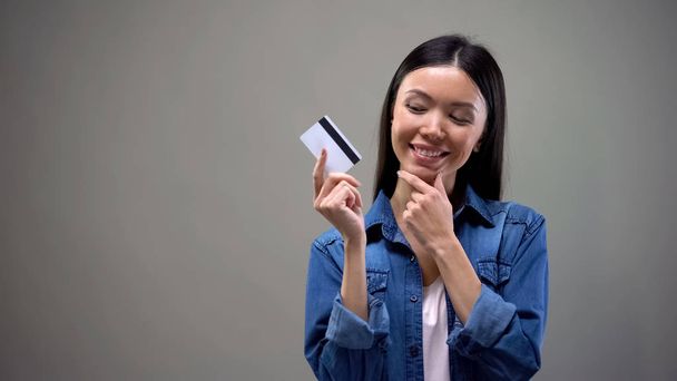 Улыбающаяся азиатка держит кредитку и думает о шоппинге, без ограничений
 - Фото, изображение