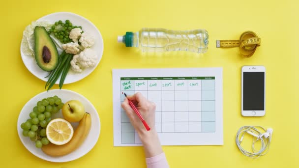 Een fitness kalender houden. concept van gezond eten, dieet, bovenaanzicht, gele achtergrond - Video
