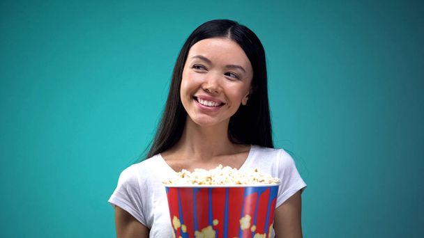Sinemada gülümseyen ve flört patlamış mısır büyük fincan ile Çekici genç kadın - Fotoğraf, Görsel