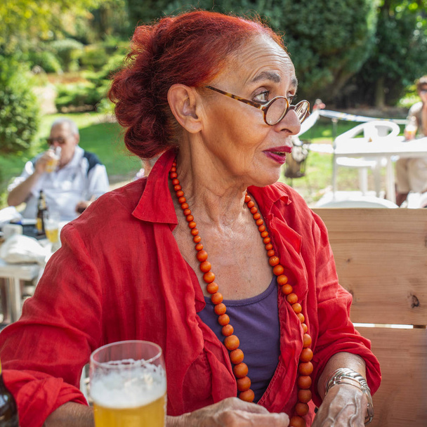 Houkutteleva muodikas 75-vuotias nainen punaisissa vaatteissa ja pyöreissä laseissa
 - Valokuva, kuva