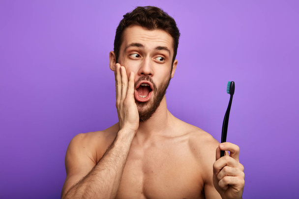 surprised man with palm on his cheek holding a toothbrush - Φωτογραφία, εικόνα