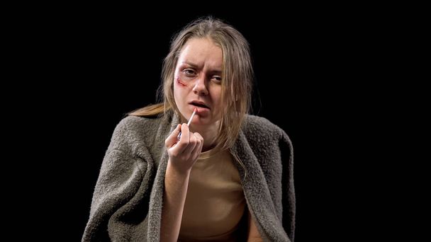 Depressed woman with wound on cheek applying lipstick, domestic violence danger - Foto, Bild