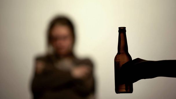 Bottle of beer in hand offering to drink alcohol, addicted woman on background - Foto, Bild