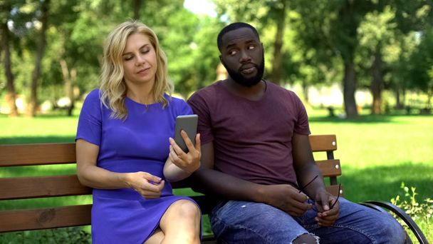 Caucasian woman playing smartphone on date in park, ignoring worried boyfriend - Photo, Image