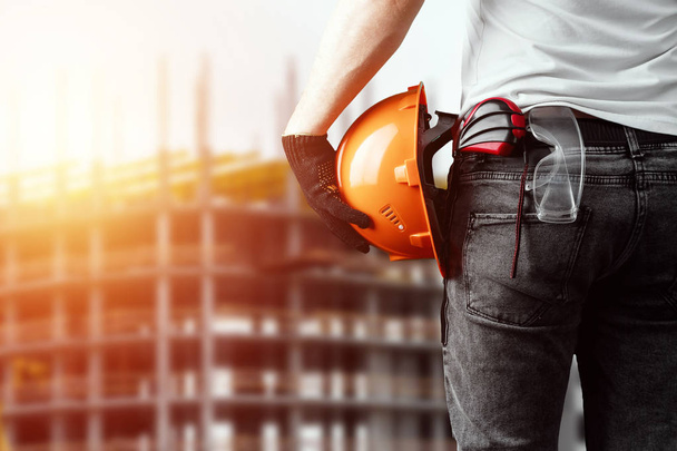 A builder, an architect holds in his hand a construction helmet against the background of a construction site, a tape measure. Concept architecture, construction, engineering, design, repair. - Foto, Imagem