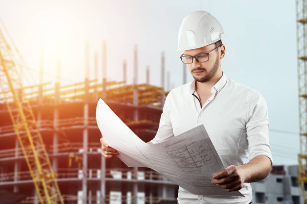 The builder, the architect holds in his hand architectural drawings on the background of the construction site. Concept architecture, construction, engineering, design, repair. Copy space - Фото, зображення