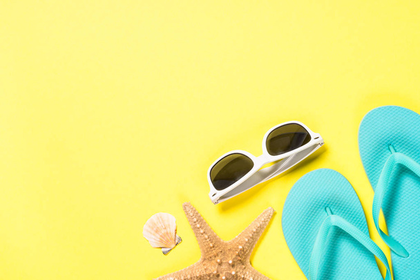 Blue flip flops, sunglasses and starfish on yellow background. - Photo, Image