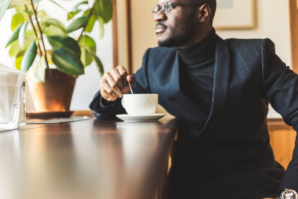 Young handsome dark-skinned businessman drinks coffee in a cafe. - Photo, image