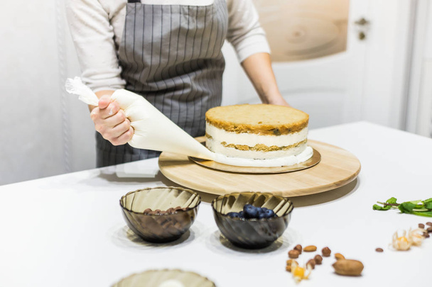 Makeiset leivonnaispussi puristamalla kerma kakku keittiössä. Käsite kotitekoinen leivonnaiset, ruoanlaitto kakut. - Valokuva, kuva