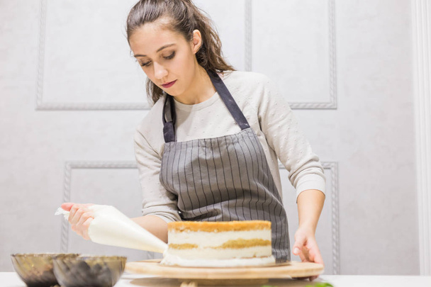 Confectioner with pastry bag squeezing cream on cake at kitchen. The concept of homemade pastry, cooking cakes. - Фото, зображення