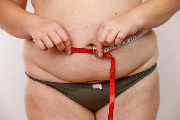 een vrouw van middelbare leeftijd met overgewicht in ondergoed meten van haar lichaam - Foto, afbeelding