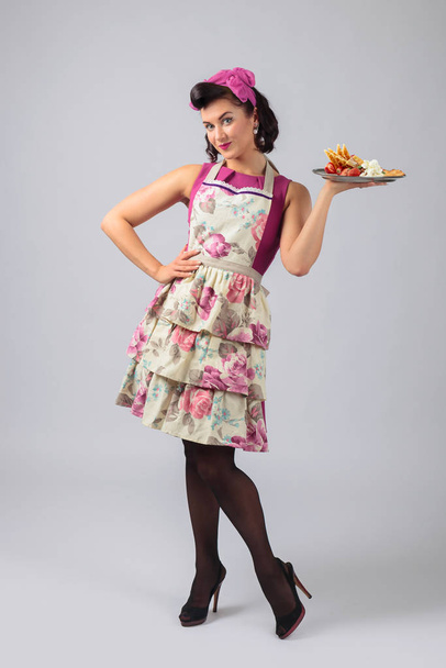 Bella giovane casalinga in abito viola e grembiule con dessert
 - Foto, immagini