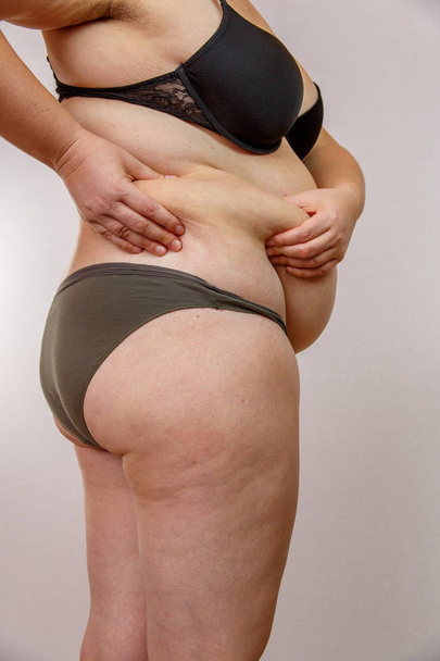žena stiskne břicho, dívka stiskne tuk na břiše, tučné záhyby na břiše - Fotografie, Obrázek