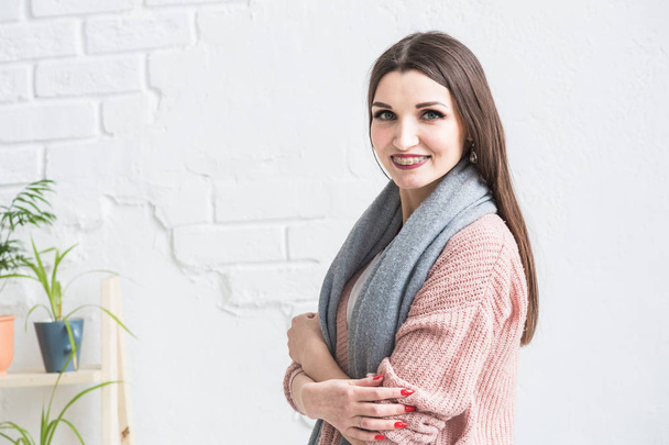 Portrait of a beautiful young brunette woman in a sweater with a scarf on a light background. - Fotoğraf, Görsel