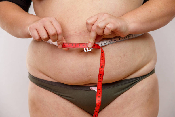 a middle-aged woman with overweight in underwear measuring her body - Foto, Imagen
