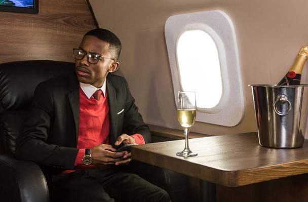 Successful young Afro American black businessman sitting in the chair of his private jet - Foto, Imagem