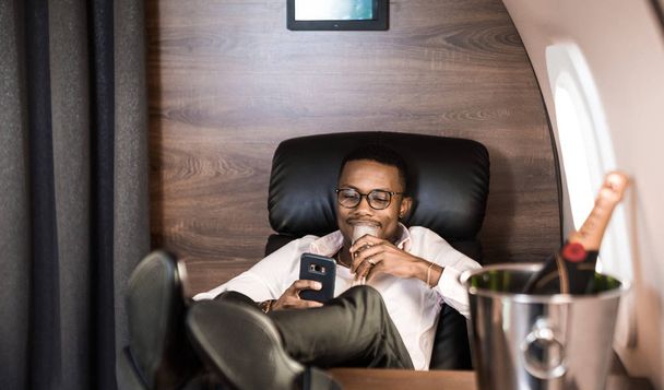 Successful young Afro American black businessman sitting in the chair of his private jet - Φωτογραφία, εικόνα