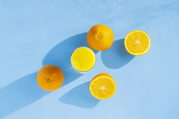 Mavi arka planda bir bardak portakal suyu ve portakal. Vitamin kavramı, tropik, yaz. Doğal ışık. Düz döşeme, üst görünüm. - Fotoğraf, Görsel