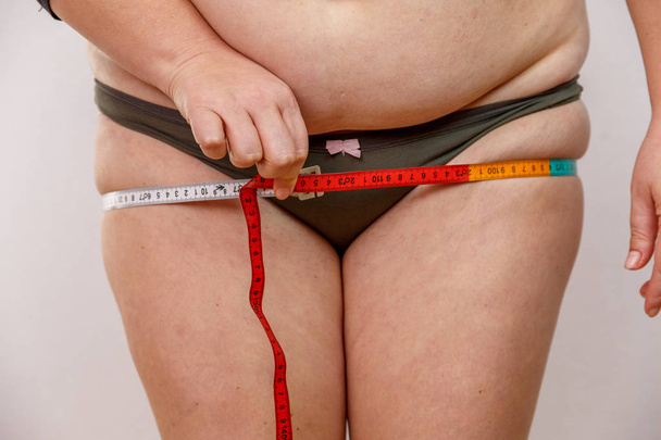 keski-ikäinen nainen, jolla on ylipaino alusvaatteissa ja joka mittaa ruumistaan
 - Valokuva, kuva